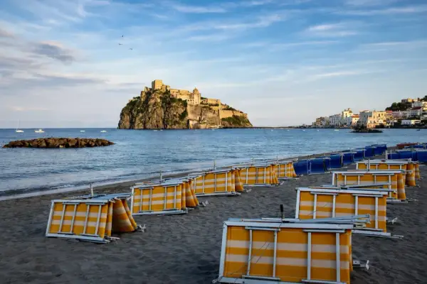 Spiaggia della Mandra a Ischia, con lettini piegati e il Castello Aragonese sullo sfondo.