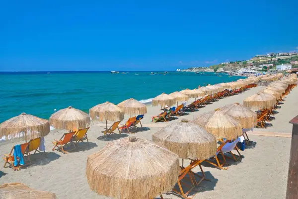 Spiaggia attrezzata con ombrelloni e lettini, mare azzurro e case in collina. Perfetto per chi cerca il **hotel San Valentino Ischia distanza dal mare** ideale.