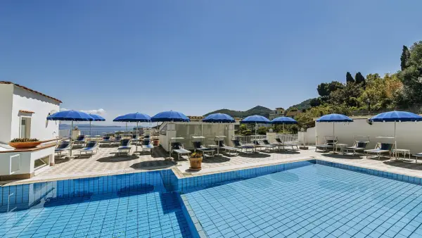 Piscina e lettini sotto ombrelloni blu al **hotel villa d'Orta Casamicciola**. Vista mare e collina.